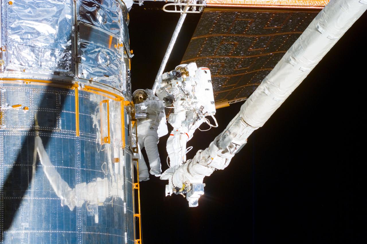 S82-E-5718 (18 Feb. 1997) --- Making use of the Remote Manipulator System (RMS) astronauts Mark C. Lee (left), STS-82 payload commander, and Steven L. Smith, mission specialist, perform the final phases of Extravehicular Activity (EVA) duty. Lee holds a patch piece for Bay #10, out of view, toward which the two were headed. A sample of the patch work can be seen on Bay #9 in the upper left quadrant of the picture. This view was taken with an Electronic Still Camera (ESC).