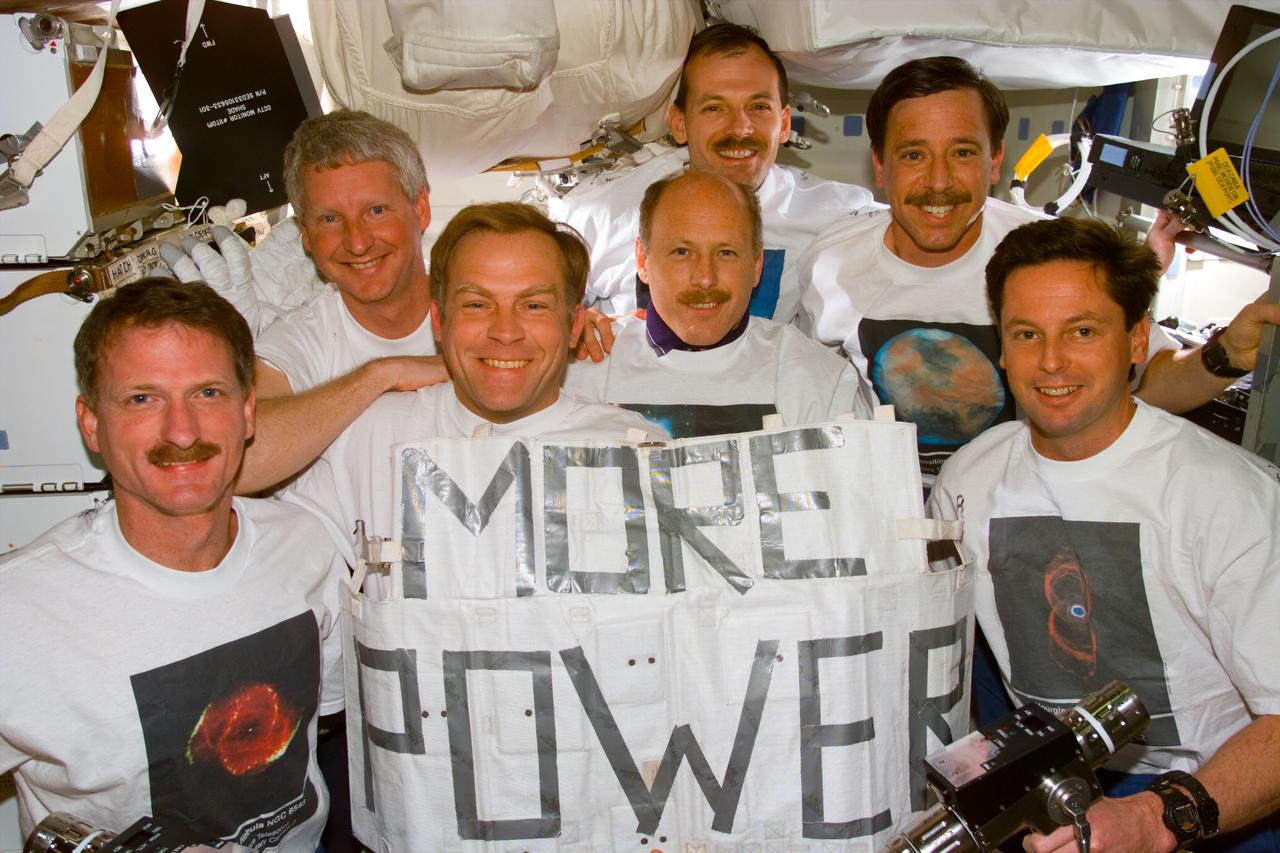 S82-E-5948 (11-21 Feb. 1997) --- The STS-82 crew poses for a traditional in-flight portrait following completion of five Extravehicular Activities (EVA) to service the Hubble Space Telescope (HST).  Both the sign held by the crew and the assortment of apparel pay tribute to the HST and its team of ground supporters.  In front, left to right, are astronauts Joseph R. Tanner, Mark C. Lee and Gregory J. Harbaugh.  Behind them, left to right, are astronauts Steven A. Hawley, Kenneth D. Bowersox and Scott J. Horowitz.  At the very back is astronaut Steven L. Smith.  Each astronaut is wearing a shirt bearing an image of a planet or other celestial body photographed originally by the giant observatory.