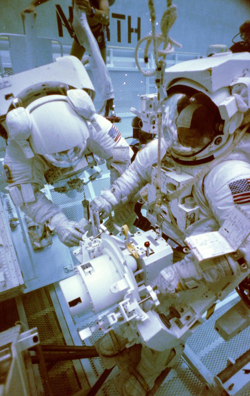 S83-42893 (19 Oct 1983) ---- Astronauts George D. Nelson and James D. van Hoften, two of three STS-41C mission specialists, share an extravehicular activity (EVA) task in this simulation of a Solar Maximum Satellite (SMS) repair visit.  The two are making use of the Johnson Space Center's (JSC) weightless environment  training facility (WET-F).  Dr. Nelson is equipped with the manned maneuvering unit (MMU) trainer and  he handles the trunion pin attachment device  (TPAD), a major tool to be used on the mission.  The photograph was taken by Otis Imboden.