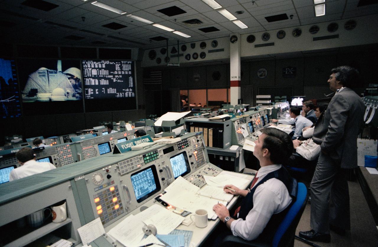 S84-26333 (6 Feb 1984) --- Robert E. Castle, integrated communications officer (INCO), is seated at the INCO console in the mission operations control room (MOCR) of Johnson Space Center's (JSC) mission control center (MCC). He is responsible for ground controlled television from the orbiter on his shift. On the screen at the front of the room the Westar VI satellite is seen in the cargo bay just after opening the payload bay doors.