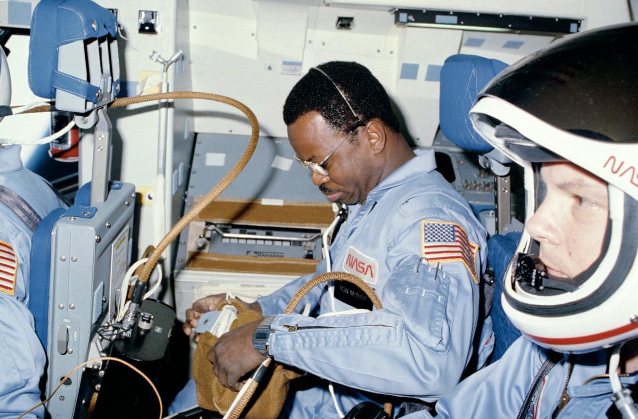 S84-27028 (3 Feb 1984) --- Astronaut Ronald E. McNair, left, and Robert L. Stewart prepare to enter an eight-day Earth-orbital mission aboard the Space Shuttle Challenger.  Photographed by Astronaut Bruce McCandless II, McNair had already moved his helmet.  Launch was less than ten minutes earlier from Launch Pad 39A at Kennedy Space Center, Florida.  The three mission specialists were joined by Astronauts Vance D. Brand, commander; and Robert L. Gibson, pilot, for the flight.  McCandless?s launch phase station is in the middeck.