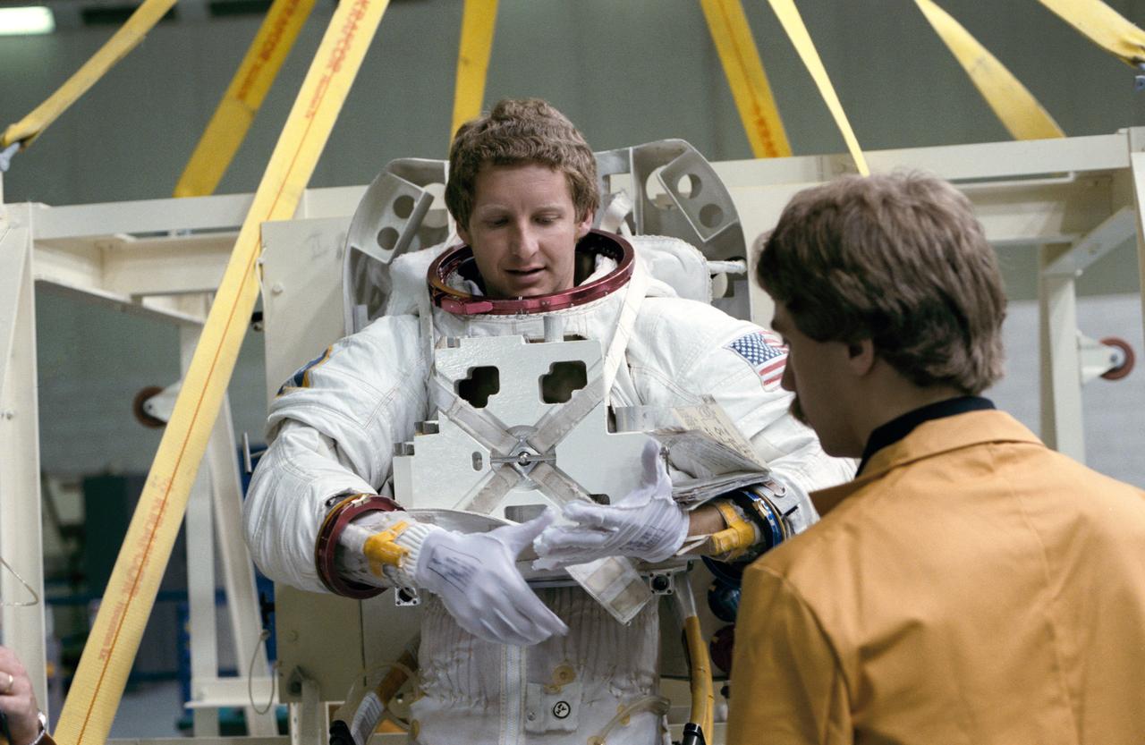 S84-28203 (24 Feb 1984) --- Astronaut Steven A. Hawley, 41-D mission specialists, completes suiting up procedures before being submerged in the Johnson Space Center's (JSC) 25 ft. deep weightless environment training facility (WET-F).  Obscured behind Dr.  Hawley is astronaut Richard M. (Mike) Mullane, 41-D mission specialist.  later the pair were lowered into the facility for an underwater simulation of a contingent extravehicular activity for the week-long flight.
