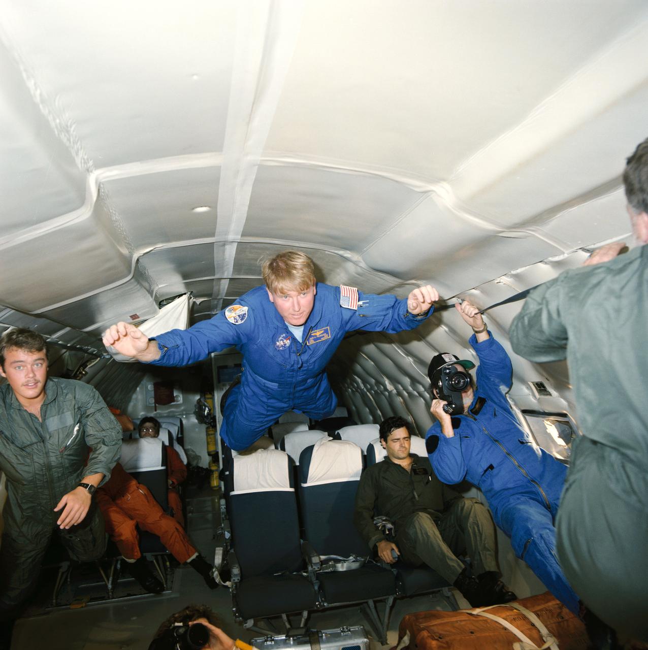 S84-37522 (18 July 1984) --- Astronaut Jon A. McBride, center, floats briefly aboard a NASA KC-135 aircraft during a flight designed as part of the training program for 41-G's seven crewmembers. McBride is pilot for that October 1984 flight. Marc Garneau, one of two payload specialists for the mission, is seated at right. Garneau represents the National Research Council of Canada.