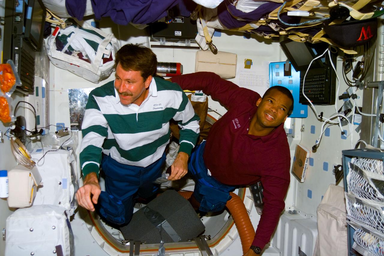 S85-E-5090 (14 August 1997) --- Astronauts Kent V. Rominger (left), pilot, and Robert L. Curbeam Jr., mission specialist, float onto the middeck of the Earth-orbiting Space Shuttle Discovery during flight day 8 activity.