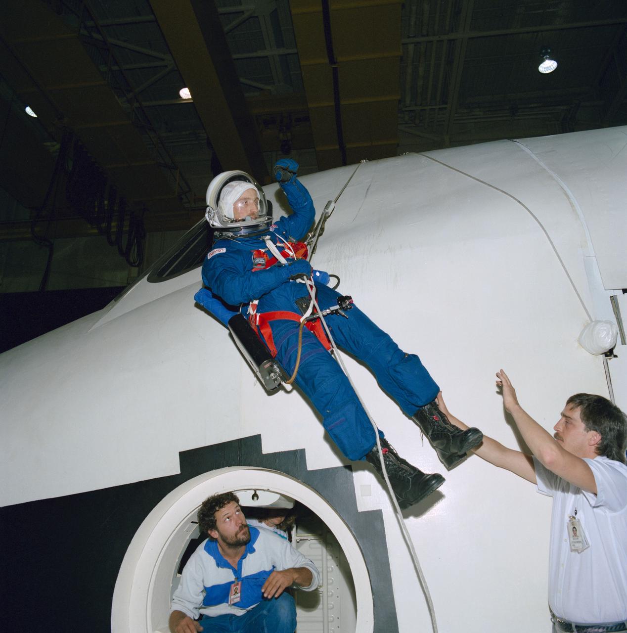 S88-38355 (27 May 1988) --- Astronaut James P. Bagian lowers himself from the top of one of the full-fuselage trainer in JSC's Shuttle mockup and integration laboratory during a post-landing, over-the-top emergency egress test.  Bagian, a M.D., and one of three mission specialists assigned to NASA STS-29 flight of the Discovery, is working with engineers evaluating egress using the new crew escape equipment that includes a parachute harness.