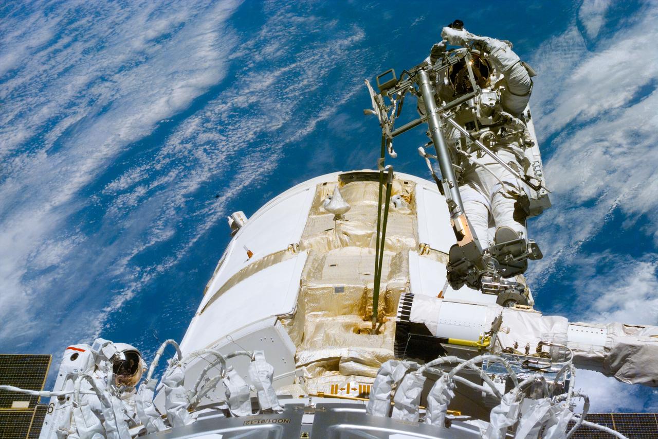S88-E-5101 (12-10-98) --- Astronaut James H. Newman, mission specialist, is backdropped against a blue and white Earth while standing on a mobile foot restraint attached to Endeavour's remote manipulator system (RMS).  Astronaut Jerry L. Ross, mission specialist, is  at left.  Part of the Russian-built Zarya module is in the center of the frame. The photo was taken with an electronic still camera (ESC) at 02:21:27 GMT, Dec. 10