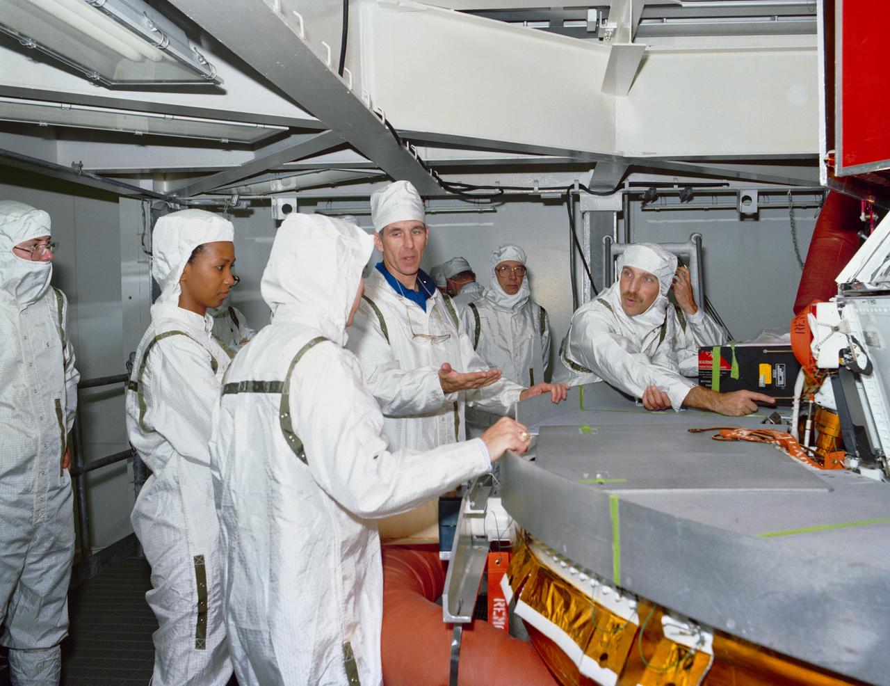 S89-28108 --- Astronaut Mae C. Jemison and STS-29 Mission Specialist  James P. Bagian and Robert C. Springer inspect the interface between the tracking and data relay satellite D (TDRS-D) and inertial upper stage (IUS-9) in a test cell located in the Kennedy Space Center (KSC) Vertical Processing Facility (VPF). The clean-suited astronauts, engineers, and technicians discuss the payload. Photo credit: NASA