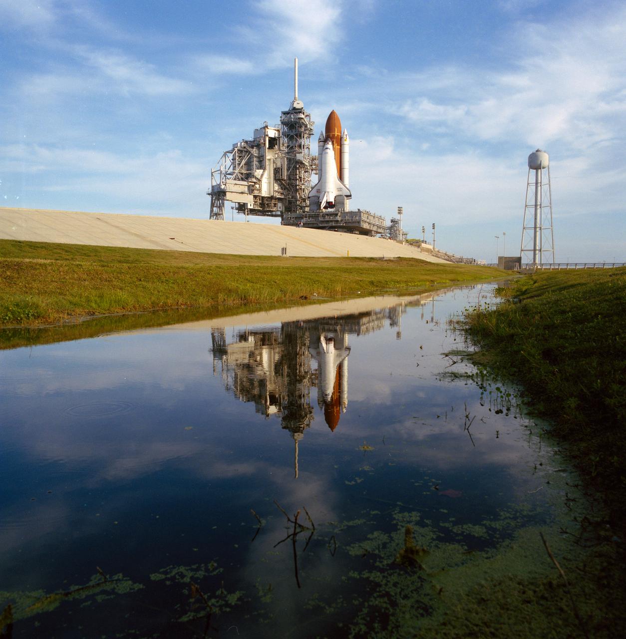 S89-30719 (22 March 1989) --- Space shuttle Atlantis is seen soon in duplicate, thanks to reflection in nearby water, after arriving at Pad 39-B. The spacecraft left the vehicle assembly building (VAB) at 12:01A.M. and arrived to this point at 7 A.M. Atlantis is scheduled for NASA STS-30 mission on which the Magellan will be deployed to orbit planet Venus and map its topographic features. Launch is scheduled for April 28.
