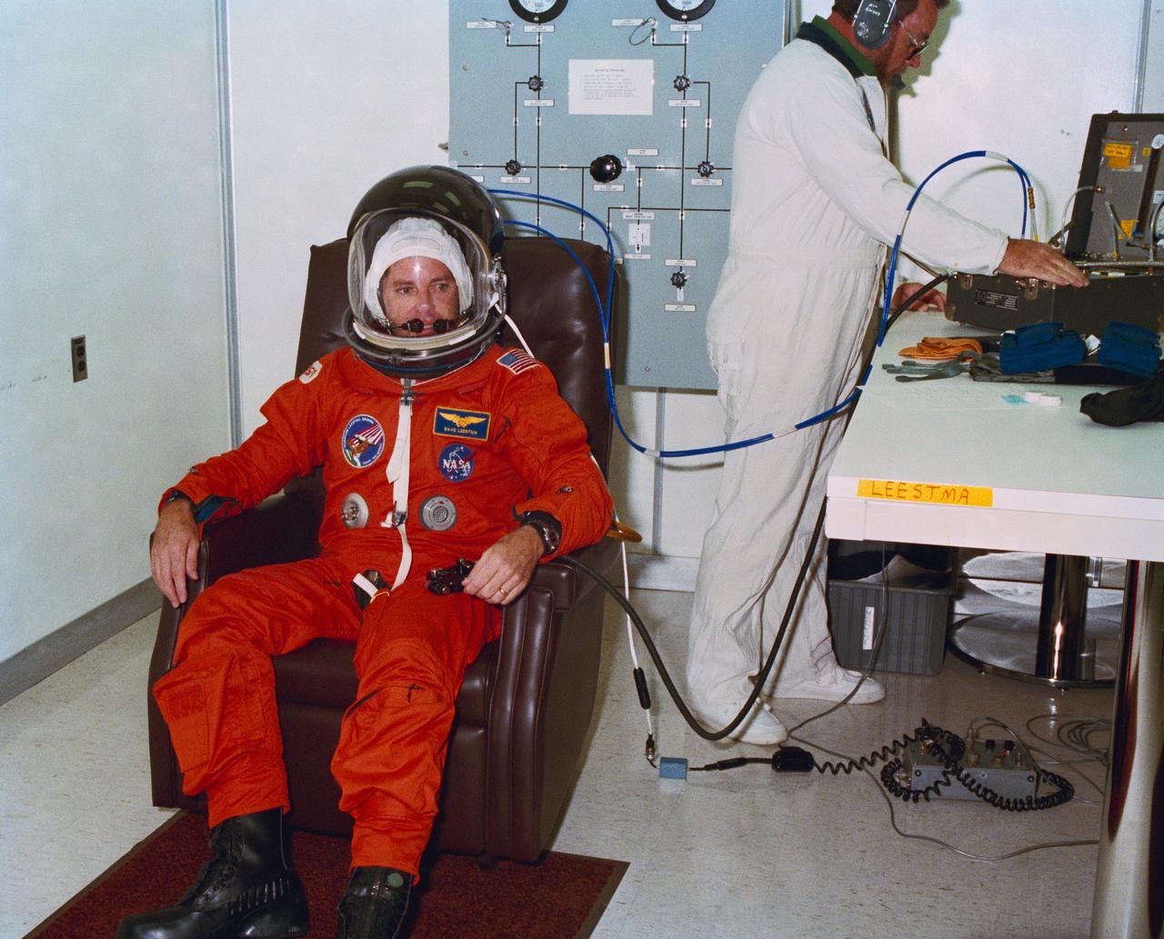 S89-41093 (9 Aug 1989) --- STS-28 Columbia, Orbiter Vehicle (OV) 102, mission specialist David C. Leestma relaxes in chair after donning launch and entry suit (LES) and launch and entry helmet (LEH). Technician in the background monitors LES systems. Leestma, along with fellow crewmembers, is participating in the terminal countdown demonstration test (TCDT) at the Kennedy Space Center (KSC) Operations and Checkout (O&C) Building. View provided by KSC with alternate number KSC-89PC-673.