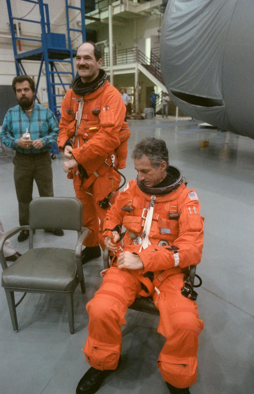 S90-28710 (12 Feb 1990) --- Astronaut Guy S. Gardner, STS-35 pilot, (standing) and Jeffrey A. Hoffman, mission specialist, prepare for egress training at the Johnson Space Center?s (JSC) Mockup and Integration Laboratory (MAIL) Bldg 9A. Gardner and Hoffman, wearing orange launch and entry suits (LES), adjust their parachute harnesses as they listen to instructions before training begins. The astronaut crewmembers and payload specialists for the scheduled May flight were specifically learning proper measures to take in the event of an emergency on the launch pad necessitating emergency evacuation of the orbiter.