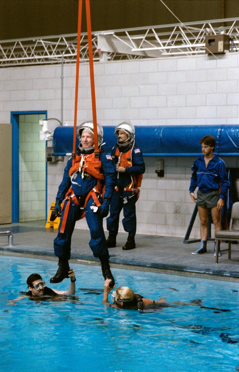S90-34964   (16 April 1990)  ---  Astronaut Vance D. Brand, STS-35 commander, is suspended via his parachute harness above the pool in the Johnson Space Center?s (JSC) Weightless Environment Training Facility (WETF) Bldg 29 during launch emergency egress exercises. Divers in the pool hold Brand's feet to steady him. In the background and on the poolside is pilot Guy S. Gardner. Both Brand and Gardner are wearing launch and entry suits (LES) and launch and entry helmets (LEH).