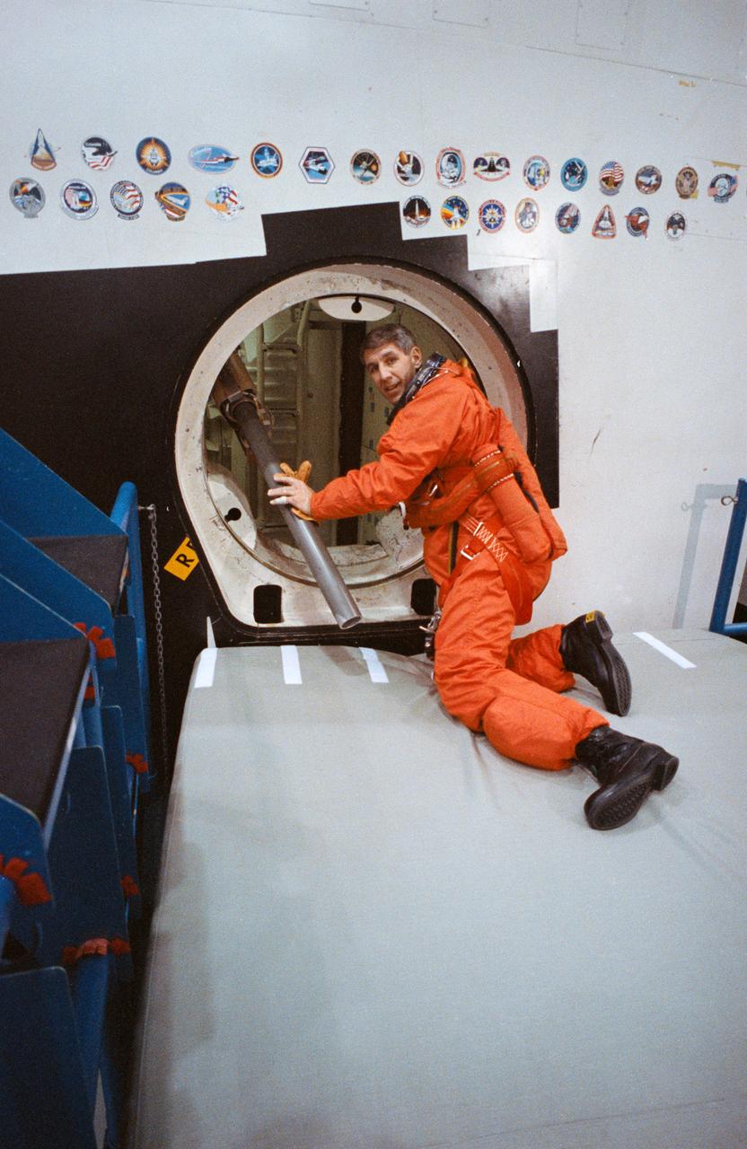 STS-38 Mission Specialist (MS) Robert C. Springer, wearing launch and entry suit (LES), climbs through the side hatch of the crew compartment trainer (CCT) located in JSC's Mockup and Integration Laboratory (MAIL) Bldg 9A. Springer will practice emergency egress through the side hatch using the crew escape system (CES) pole (at Springer's left). The inflated safety cushion under Springer will break his fall as he rolls out of the side hatch.