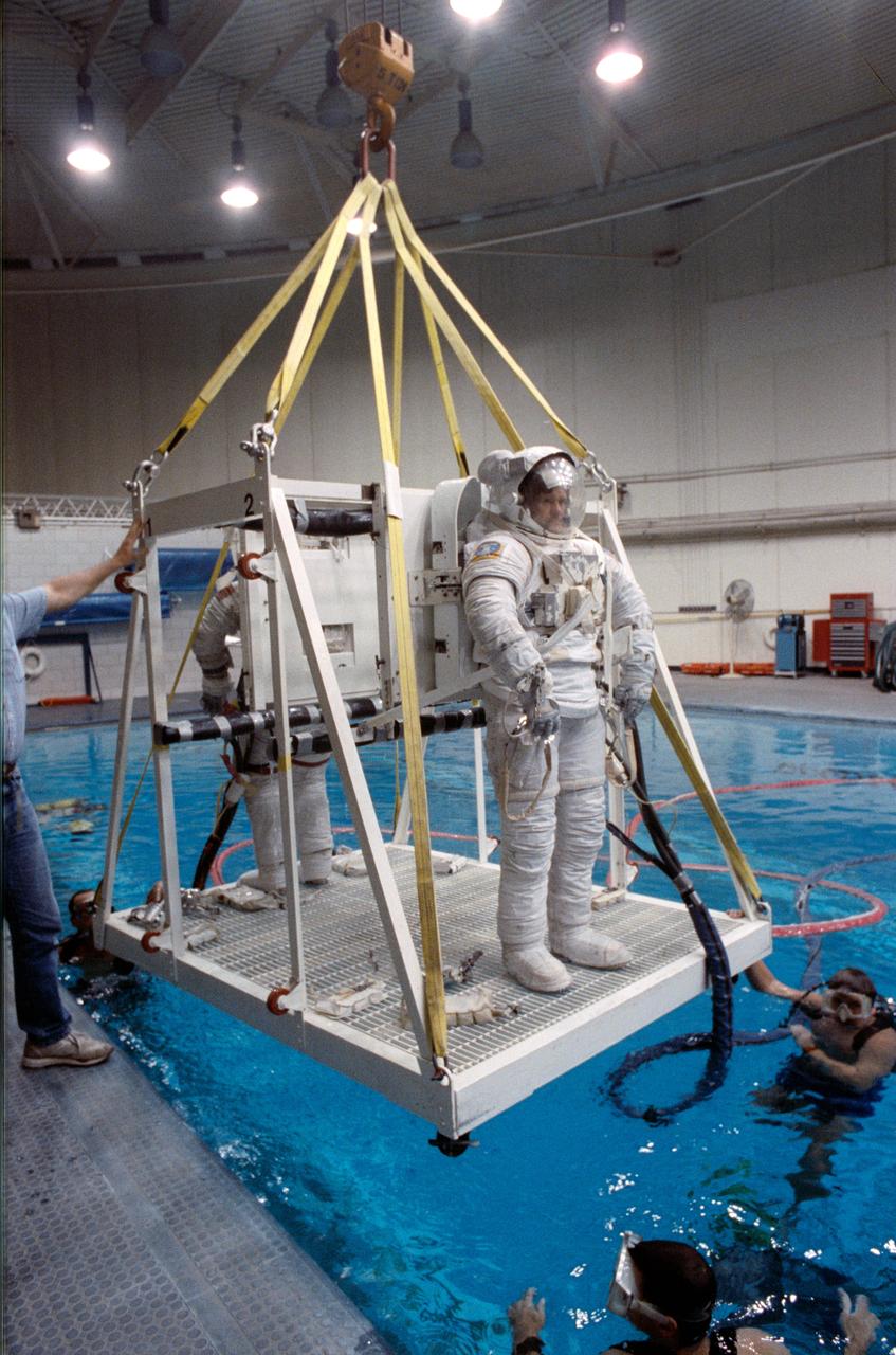 S90-46030 (Aug 1990) --- Astronaut Donald R. McMonagle (foreground) wears an extravehicular mobility unit (EMU) spacesuit as he prepares to be lowered into a 25-ft. deep pool at the Johnson Space Center's weightless environment training facility (WET-F). Astronaut Gregory J. Harbaugh, a fellow STS 39 mission specialist, shares the moveable platform with McMonagle and prepares to join him in the simulation of a contingency extravehicular activity (EVA) for the mission, scheduled for Discovery in the spring of 1991. A number of SCUBA-equipped divers assist in the training session.