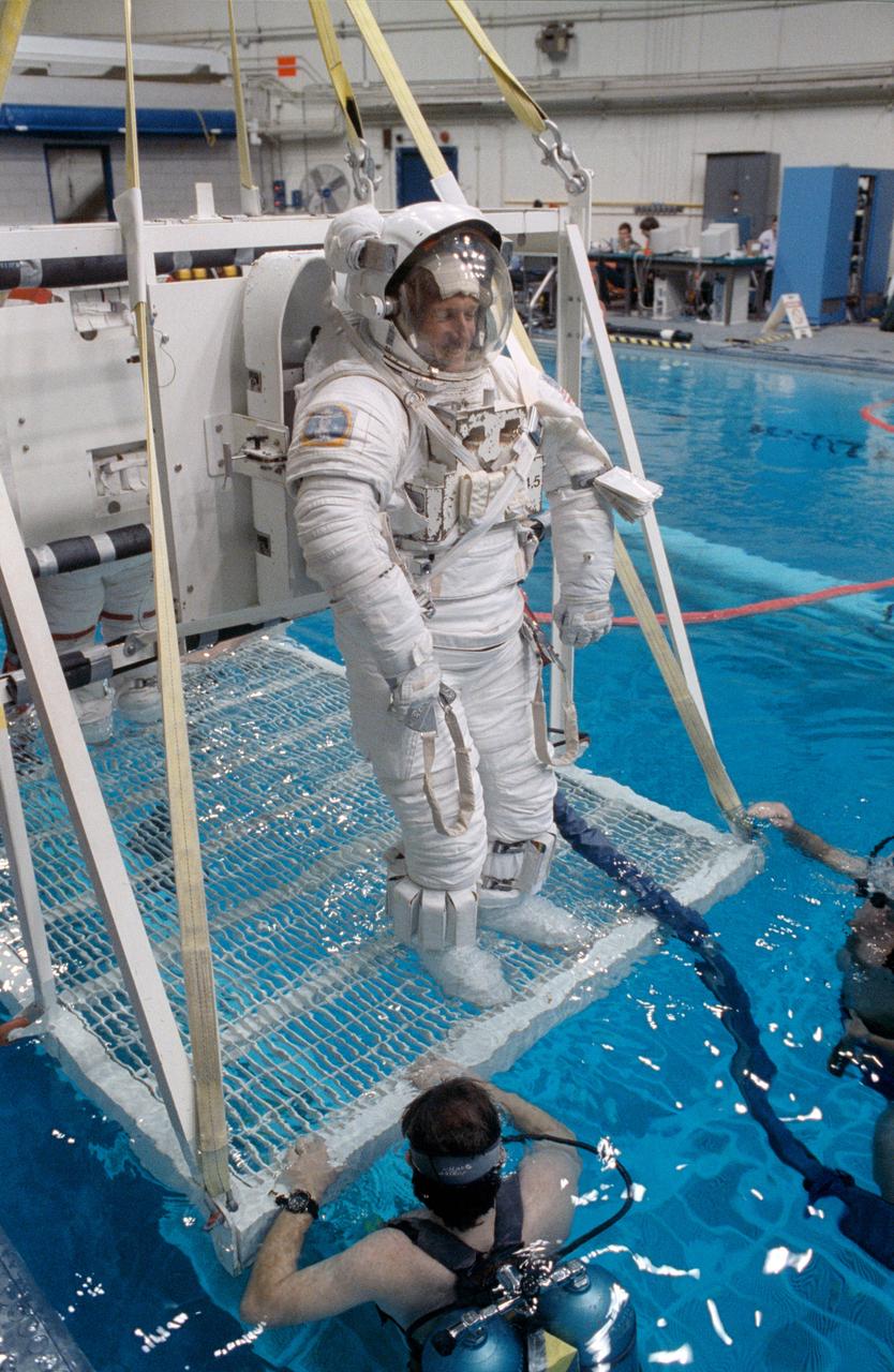 S91-30197 (1 March 1991) --- A wider shot of astronaut C. Michael Foale, mission specialist, standing on a platform which is part of a system that will lower him into a 25-ft. deep pool. Foale used the pool in the weightless environment training facility (WET-F) to rehearse a contingency extravehicular activity (EVA). Two SCUBA-equipped swimmers assist. Astronauts wear pressurized spacesuits configured for achieving a neutrally buoyant condition in the water to simulate both planned and contingency EVAs.