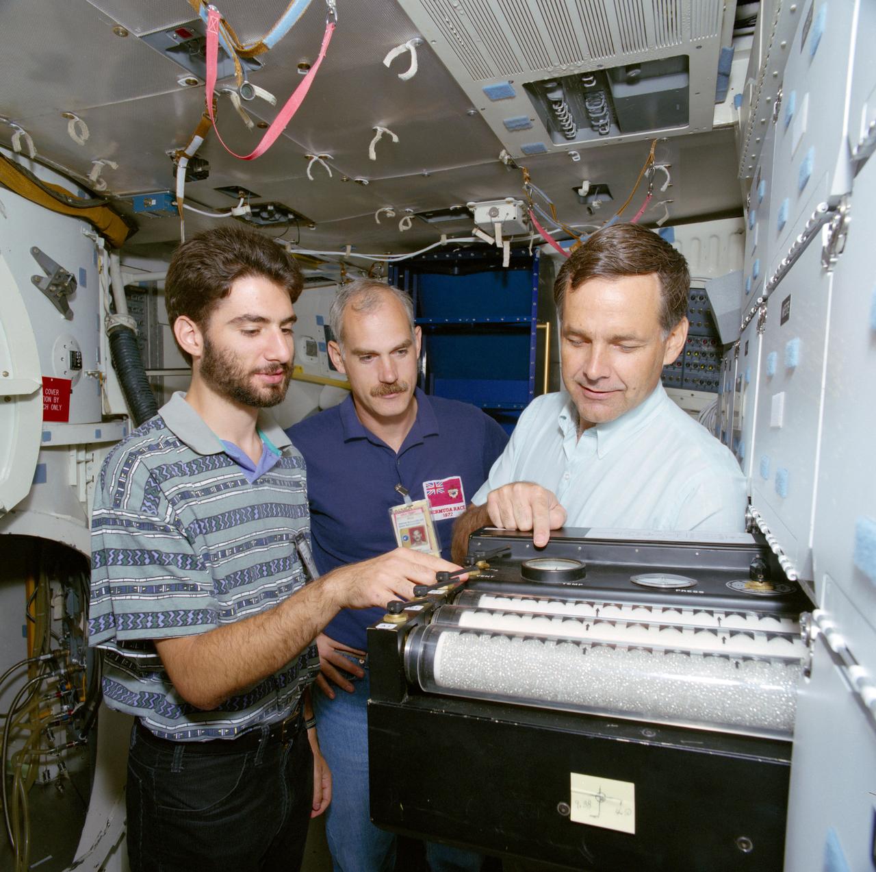S91-47323 (18 Sept 1991) --- Constantine Costes, left, a student experimenter sponsored by United Space Boosters Inc, in Huntsville, Alabama, discusses his student experiment, "Zero-G Rise of Liquid Through Porous Media" with astronauts Ronald J. Grabe (right), STS 42 mission commander; and  William Readdy, mission specialist. The student experimenter and crew members are in the Full Fuselage Trainer (FFT) in the Shuttle Mockup and Integration Laboratory.  While attending Randolph School, a high school in Huntsville, Alabama, Costes was chosen in the national competition to participate in the Shuttle Student Involvement Program (SSIP).  The experiment, contained in a middeck locker, involves the investigation of the effects of gravity on the flow characteristics of a fluid.  Both pure capillary and forced flow behavior will be investigated.  A ground based experiment was conducted so that gravity influenced data can be compared to that gathered in weightlessness.  Costes is now a candidate for a Ph.D in mathematics at Harvard University.