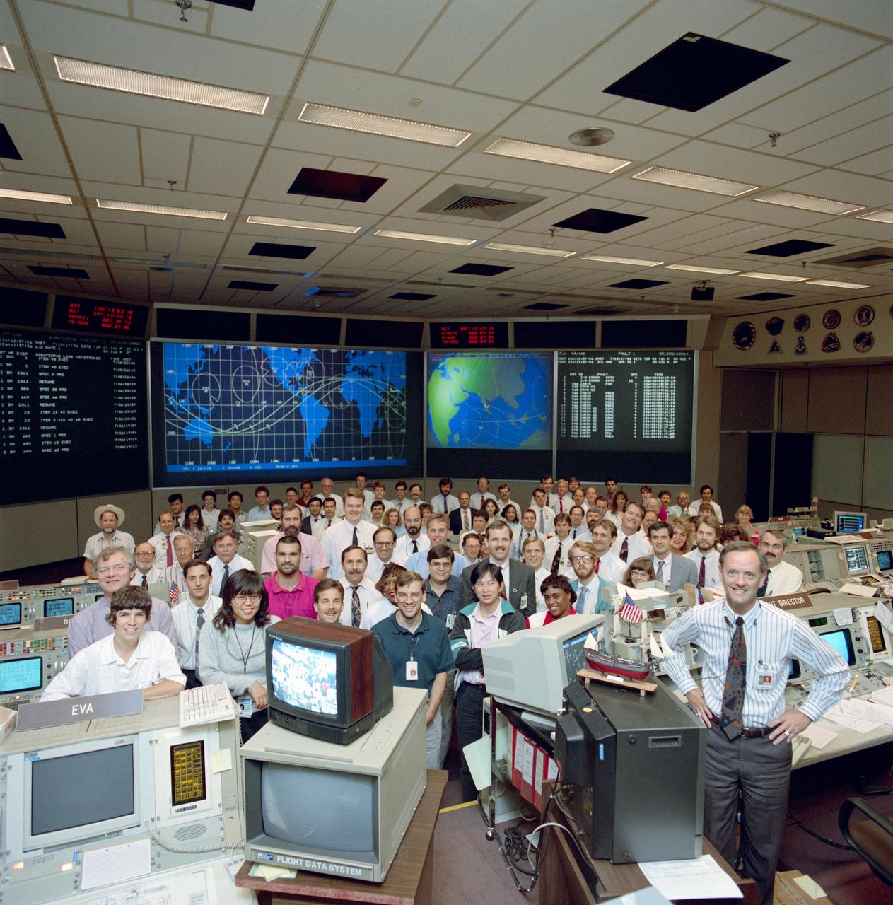 S92-36606 (20 May 1992) --- STS-49 Endeavour, Orbiter Vehicle (OV) 105, Planning Team with Flight Director (FD) James M. Heflin, Jr. (front right next to ship model) poses in Johnson Space Center?s (JSC) Mission Control Center (MCC) Bldg 30 Flight Control Room (FCR). The group stands in front of visual displays projecting STS-49 data and ground track map.