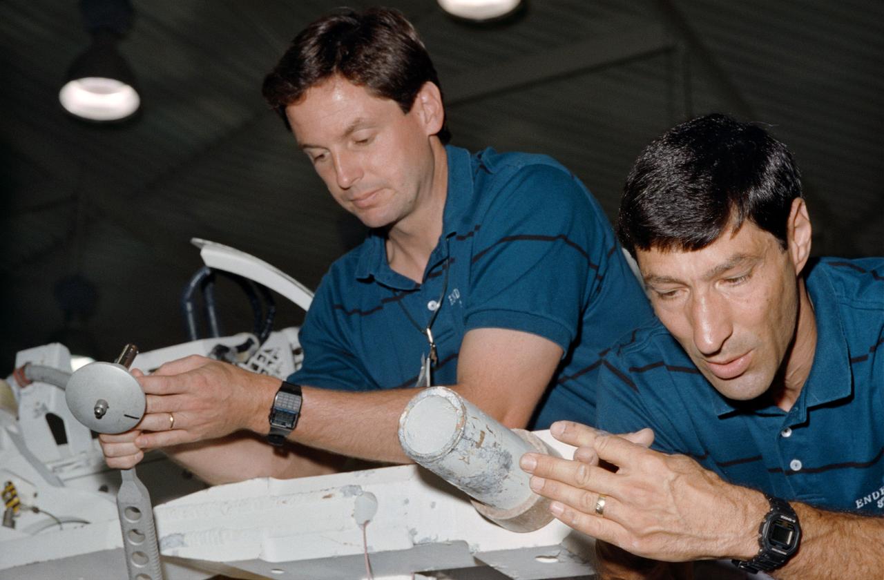 STS-54 Endeavour, Orbiter Vehicle (OV) 105, Mission Specialist 1 (MS1) Mario Runco, Jr (right) and MS2 Gregory J. Harbaugh, holding an ESSEX wrench, examine mockup and tools prior to an underwater simulation in JSC's Weightless Environment Training Facility (WETF) Bldg 29 pool. Runco and Harbaugh discuss the trunnion / payload retention latch assembly (PRLA) configuration.