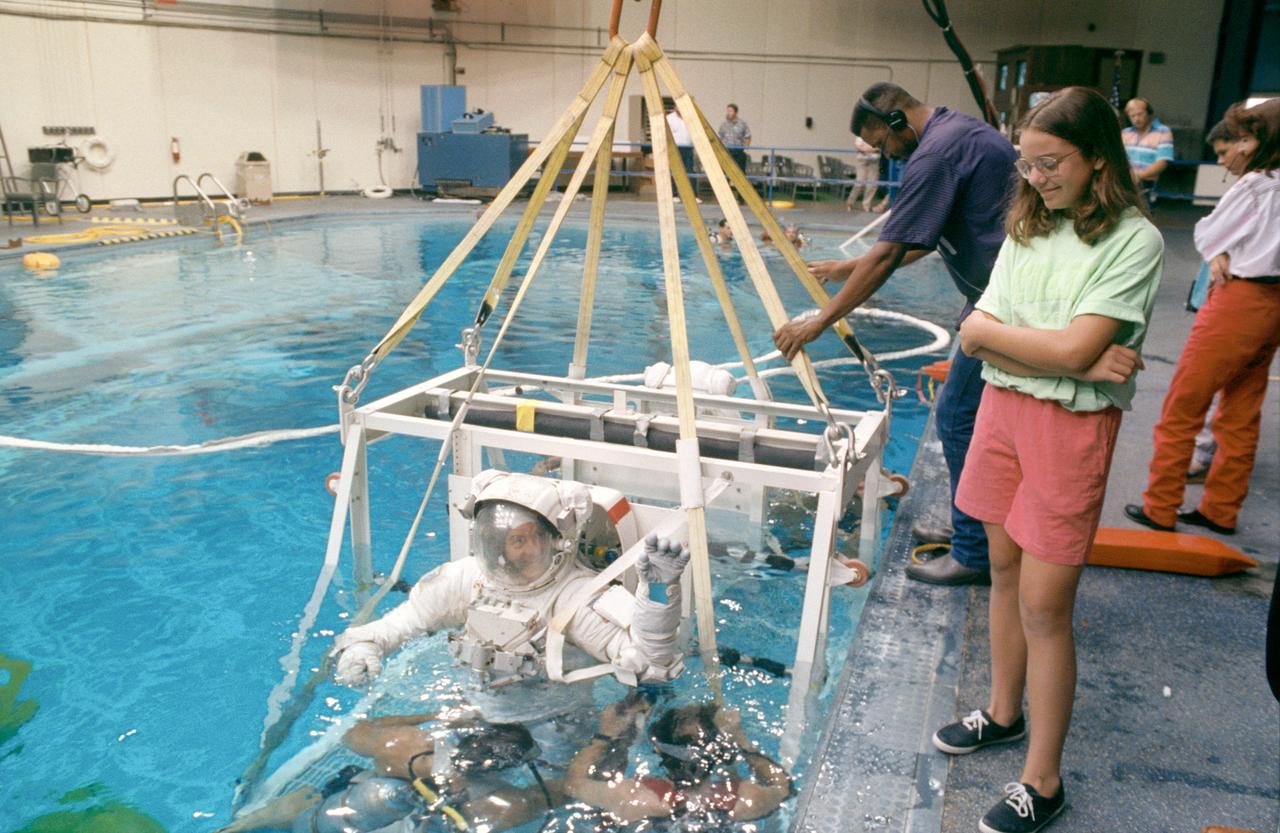 S92-43335 (28 July 1992) --- STS-53 Discovery, Orbiter Vehicle (OV) 103, Mission Specialist James S. Voss, wearing extravehicular mobility unit (EMU), is lowered into JSC?s Weightless Environment Training Facility (WETF) Bldg. 29 pool. Voss waves to his daughter standing on the poolside as the platform he is positioned in is submerged in the pool. Technicians on the poolside and scuba equipped divers in the water monitor activities. Once underwater, Voss will participate in contingency extravehicular activity (EVA) procedures.