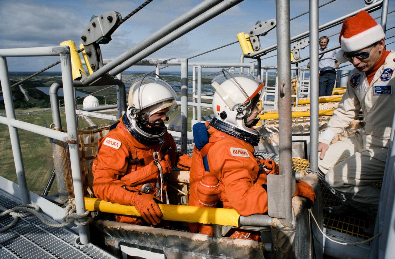 S93-25030 (15 Dec 1992) --- Two astronauts assigned to fly aboard Endeavour for the STS-54 mission are briefed on the slidewire escape system at the launch pad. Pictured in the slidewire litter are astronauts Gregory J. Harbaugh (left) and Susan J. Helms, mission specialists. They are assisted by Max Kandler of Lockheed, Houston. All five crewmembers are in Florida this week to participate in countdown demonstration tests.