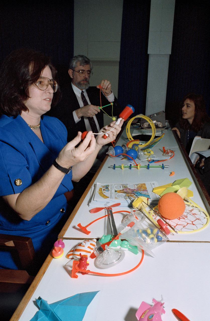 S93-25649 (6 Jan 1993) --- Carolyn Sumners, Ed.D., project director for Toys in Space, demonstrates some of the toys to be carried aboard the Space Shuttle Endeavour for the STS-54 mission later this month.  Gregory Vogt, Ed.D., NASA education specialist, is seen showing another of the toys to news media representatives here for the pre-flight press briefing.  The detailed supplementary objective (DSO-802) will allow the Shuttle crewmembers to experiment with the various types of toys in a microgravity environment while talking to pupils who will be able to monitor (via classroom TV sets) the activities at a number of schools.