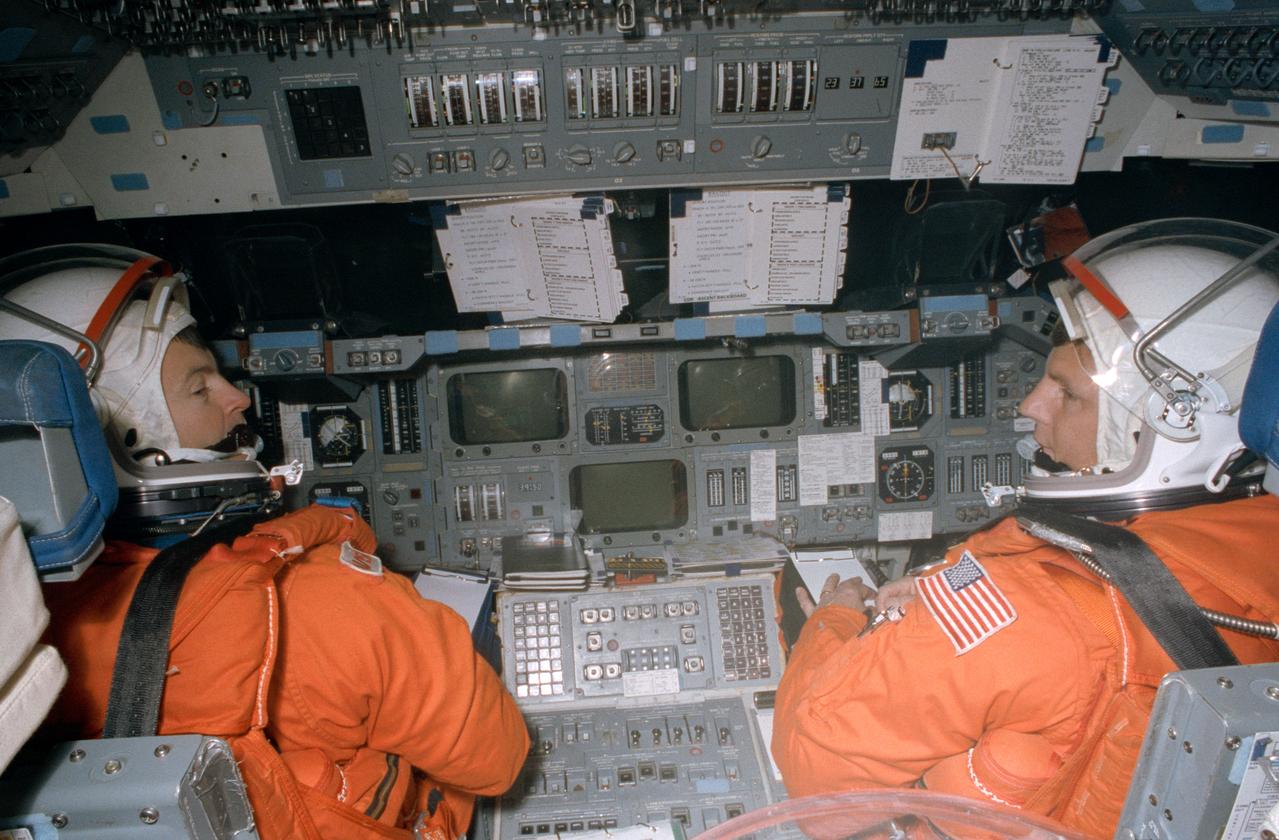 STS-56 Discovery, Orbiter Vehicle (OV) 103, Commander Kenneth Cameron, (left) and Pilot Stephen S. Oswald, wearing launch and entry suits (LESs) and launch and entry helmets (LEHs), are seated on the forward flight deck of the crew compartment trainer (CCT), a shuttle mockup. Cameron mans the commander station controls and Oswald the pilots station controls during an emergency egress (bailout) simulation. The view was taken from the aft flight deck looking forward and includes Cameron's and Oswald's profiles and the forward flight deck controls and checklists. The CCT is located in JSC's Mockup and Integration Laboratory (MAIL) Bldg 9NE.
