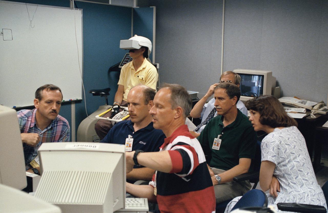 Astronaut Jeffrey A. Hoffman, one of four crewmembers for STS-61 that will conduct scheduled spacewalks during the flight, wears a special helmet and gloves designed to assist in proper positioning near the telescope while on the end of the robot arm. Crewmembers are utilizing a new virtual reality training aid which assists in refining positioning patterns for Space Shuttle Endeavour's Remote Manipulator System (RMS) (36890); Astronaut Claude Nicollier looks at a computer display of the Shuttle's robot arm movements as Thomas D. Akers and Kathryn C. Thornton, mission specialists look on. Nicollier will be responsible for maneuvering the astronauts while they stand in a foot restraint on the end of the RMS arm (36891,36894); Hoffman wears a special helmet and gloves designed to assist in proper positioning near the telescope while on the end of the robot arm (35892); Nicollier looks at a computer display of the Shuttle's robot arm movements as Akers looks on (36893); While (l-r) Astronauts Kenneth Bowersox, Kathryn Thornton, Richard O. Covey and Thomas D. Akers watch, Nicollier moves the Robot arm to desired locations in the Shuttle's payload bay using the Virtual Reality program (36895); Bowersox takes his turn maneuvering the RMS while mission specialist Hoffman, wearing the Virtual Reality helmet, follows his own progress on the end of the robot arm. Crewmembers participating during the training session are (l-r) Astronauts Akers, Hoffman, Bowersox, Nicollier, Covey, and Thornton. In the background, David Homan, an engineer in the JSC Engineering Directorate's Automation and Robotics Division, looks on (36896).