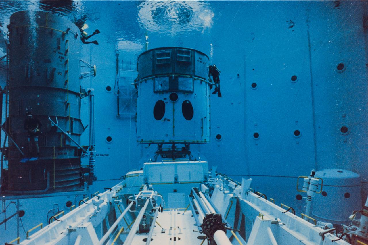Safety divers in the Neutral Buoyancy Simulator (NBS) at the Marshall Space Flight Center (MSFC) prepare a mockup of the Hubble Space Telescope (HST) for one of 32 separate training sessions conducted by four of the STS-61 crew members in June. The three-week process allowed mission trainers to refine the timelines for the five separate spacewalks scheduled to be conducted on the actual mission scheduled for December 1993. The HST is separated into two pieces since the water tank depth cannot support the entire structure in one piece. The full length payload bay mockup shows the Solar Array Carrier in the foreground and the various containers that will house replacement hardware that will be carried on the mission.