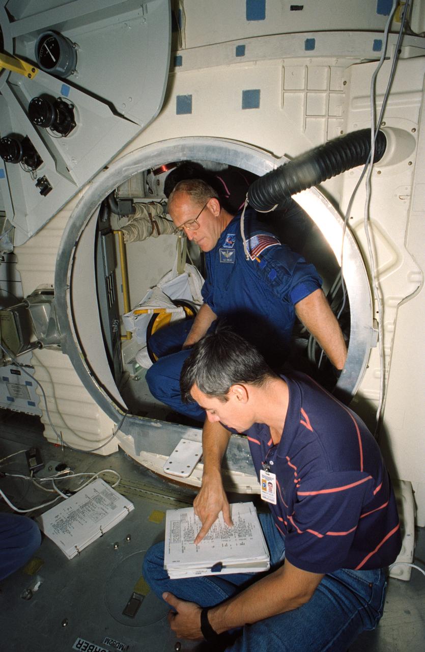 Astronauts Charles D. (Sam) Gemar, and Andrew M. Allen participate in a training exercise at JSC's Crew Compartment Trainer (CCT), located in the Shuttle mockup and integration laboratory. Gemar sits inside the airlock as Allen reviews procedures for EVA.