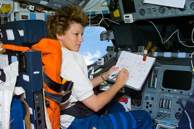 NASA image: Collins consults a checklist in the commander's seat