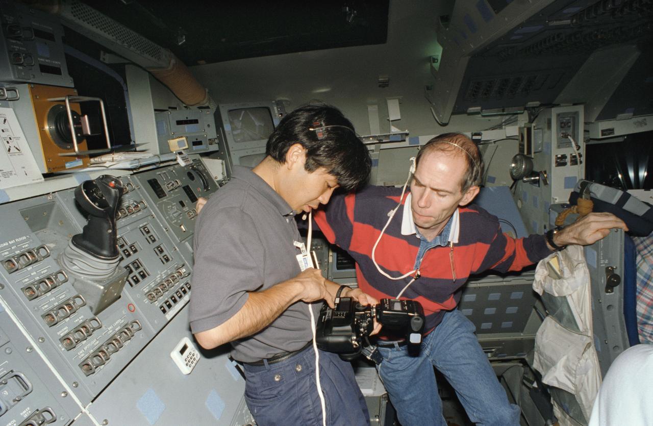 S95-12703 (May 1995) --- Astronauts Koichi Wakata (left) and Daniel T. Barry check the settings on a 35mm camera during an STS-72 training session. Wakata is a mission specialist, representing Japan's National Space Development Agency (NASDA) and Barry is a United States astronaut assigned as mission specialist for the same mission.  The two are on the aft flight deck of the fixed base Shuttle Mission Simulator (SMS) at the Johnson Space Center (JSC).