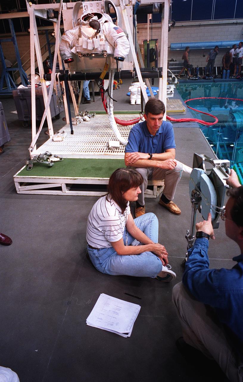S95-21276 (September 1995) --- Astronaut Linda M. Godwin, mission specialist, is briefed on the Mobile Foot Restraint (MFR) to be used in a scheduled Extravehicular Activity (EVA) during the March mission.  Astronaut Ronald M. Sega, mission specialist, looks on.  Astronaut Michael R. (Rich) Clifford, mission specialist, who will join Godwin on the EVA, is out of frame.  Godwin and Clifford checked out the hardware before donning training versions of the Extravehicular Mobility Unit (EMU) spacesuit (see torso piece in background) in preparation for being submerged in a 25-feet deep pool at the Johnson Space Center's (JSC) Weightless Environment Training Facility (WET-F).
