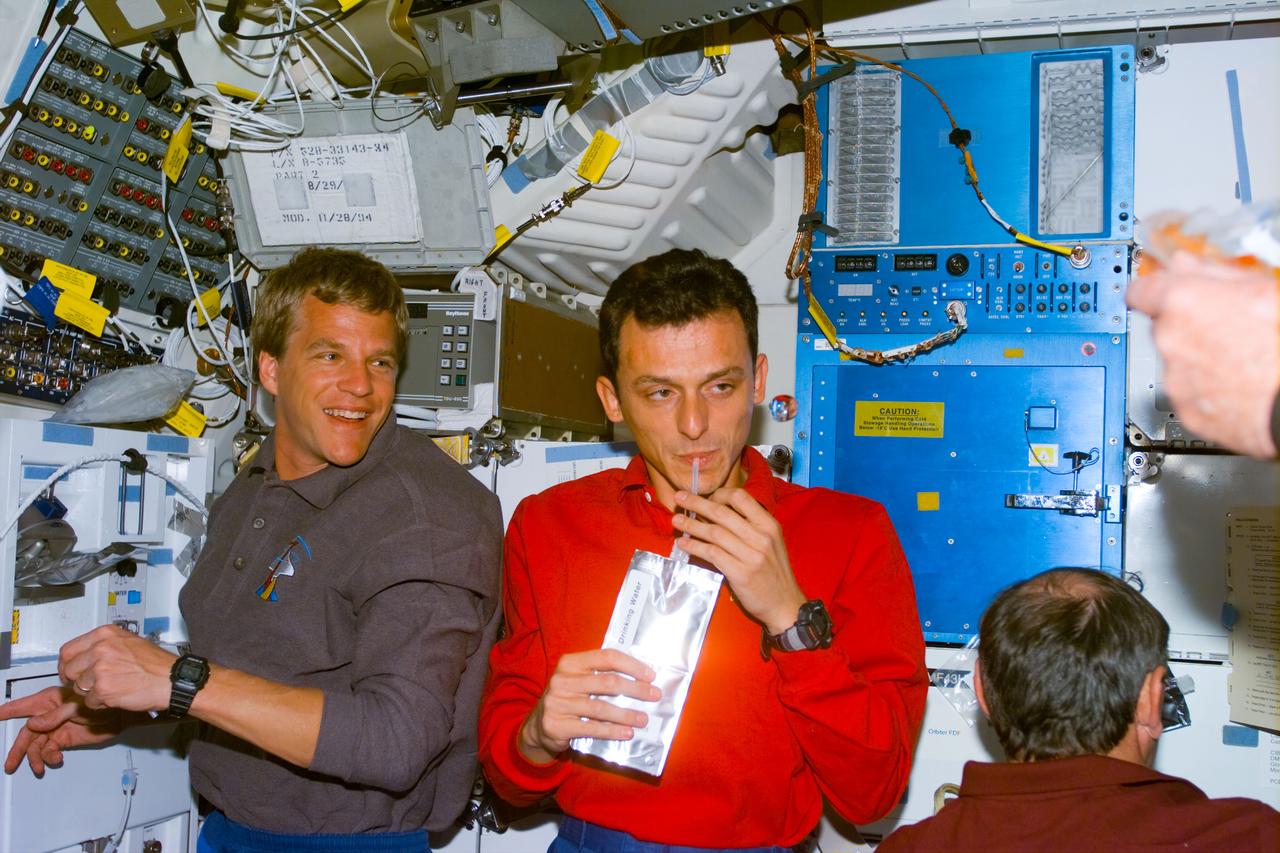 S95-E-5004 (29 Oct. 1998) --- Astronauts Scott E. Parazynski (left) and Pedro Duque, both STS-95 mission specialists, look toward astronaut Curtis L. Brown, commander, on Discovery's middeck during flight day one activity. Parazynski stands next to the galley, which Duque, who represents the European Space Agency (ESA), used to rehydrate the beverage container he holds. The photo was made with an electronic still camera (ESC) at 10:05:27 GMT, Oct. 29.