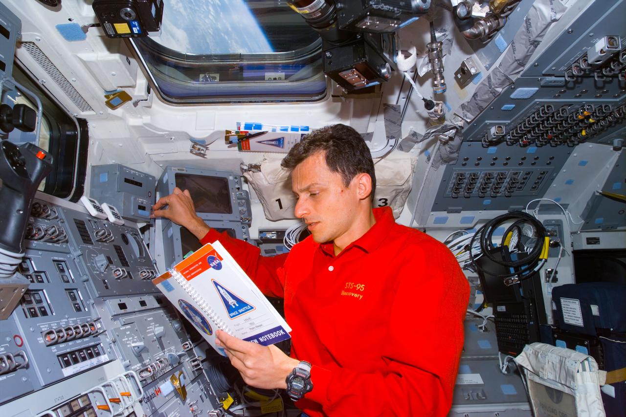 STS095-E-5027 (10-29-98) Astronaut Pedro Duque, mission specialist representing the European Space Agency (ESA)looks over notes on the Discovery's aft flight deck during Flight Day 1 activities. At left frame are controls for the remote manipulator system (RMS) and part of the frame of one of the windows overlooking the cargo bay, where the Spartan 201 satellite is berthed. The photo was taken at 11:30:18 GMT, Oct. 29.