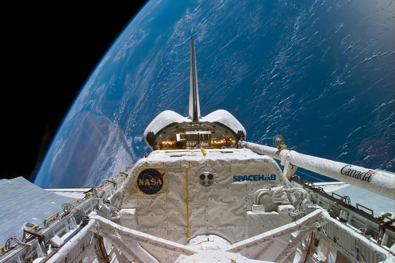 STS095-E-5030 (10-29-98) --- Backdropped  over a shoreline and thousands of miles of ocean waters, the Space Shuttle Discovery orbits Earth at 17,500 miles per hour.  In the cargo bay are the Spacehab facility and the Spartan 201 (partially obscured behind the Spacehab).  Awaiting its duties with the Spartan is the Canadian-built remote manipulator system (RMS) robot arm in its berthed configuration at right. The   scene was taken with an electronic still camera (ESC) at 11:34:13 GMT, Oct. 29.