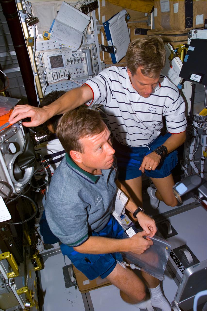 STS095-E-5111 (2 Nov. 1998) --- A high-angle view shows astronauts Steven W. Lindsey (left), STS-95 pilot, and Scott E. Parazynski, mission specialist, work with supportive gear for experiments on Spacehab. The heavily used glove box facility is on left side of frame. The photo was taken with an electronic still camera (ESC) at 05:11:38 GMT, Nov. 2.