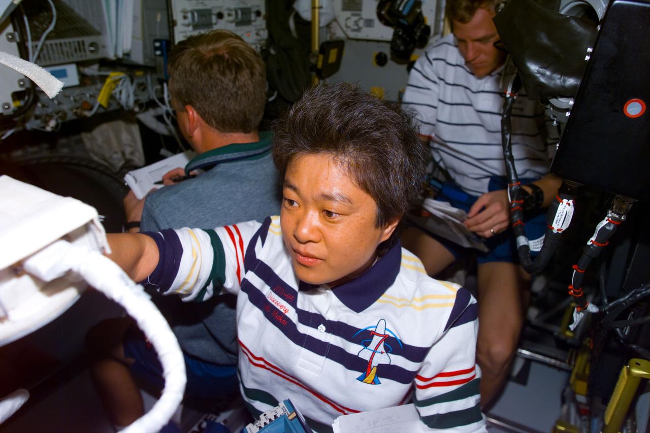 STS095-E-5115 (2 Nov. 1998) --- Payload specialist Chiaki Mukai, representing Japan's National Space Development Agency (NASDA), sets up an experiment on Spacehab during flight day four activity. In the background are astronauts Steven W. Lindsey, STS-95 pilot, and Scott E. Parazynski, mission specialist. The photo was taken with an electronic still camera (ESC) at 05:14:24 GMT, Nov. 2.