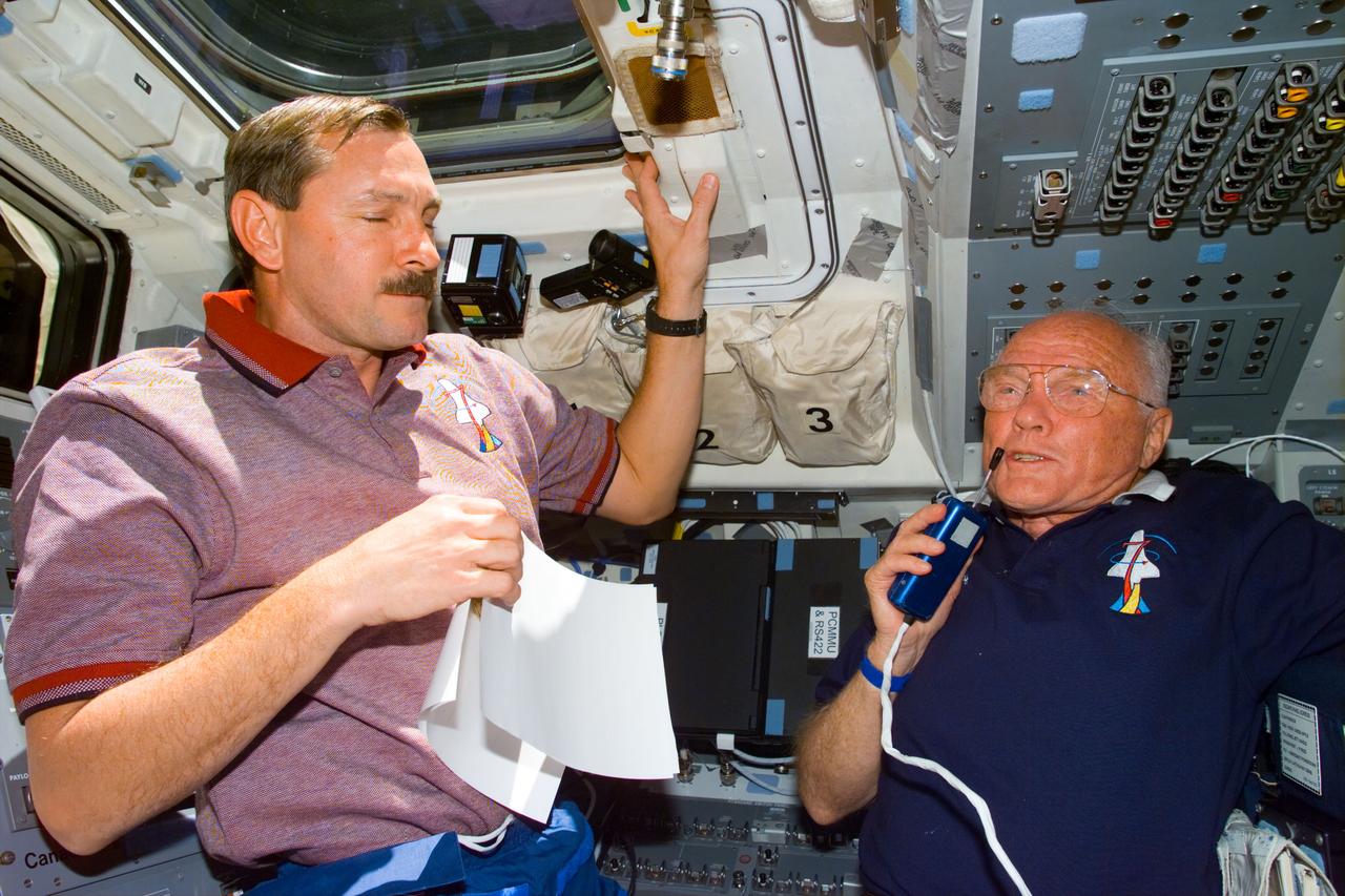 STS095-E-5180 (31 Oct. 1998) --- Astronaut Curtis L. Brown Jr. (left), STS-95 commander, stands by on Discovery's aft flight deck as U.S. Sen. John H. Glenn Jr., payload specialist, talks with ground controllers in Houston. The photo was taken with an electronic still camera (ESC) at 00:48:48 GMT, Oct. 31.