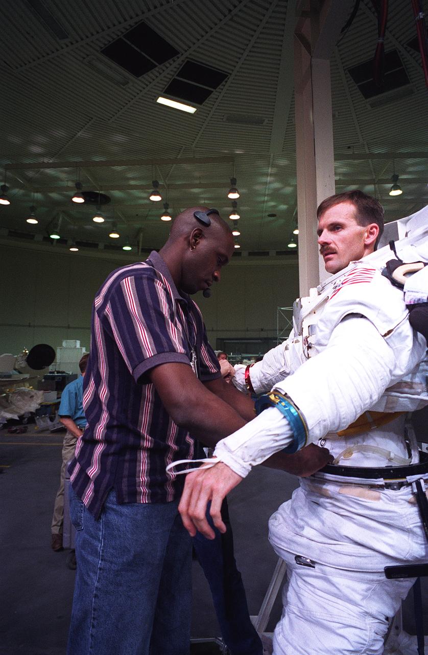 S96-11810 (10 June 1996) --- Astronaut Steven L. Smith, STS-82 mission specialist assigned to extravehicular activity (EVA) involved with the servicing of the Hubble Space Telescope (HST), gets help with the final touches of suit donning from John Williams, an Extravehicular Mobility Unit (EMU) technician.  Minutes later, Smith was underwater in a nearby tank and neutrally buoyant, rehearsing some of the HST servicing chores with a crewmate.