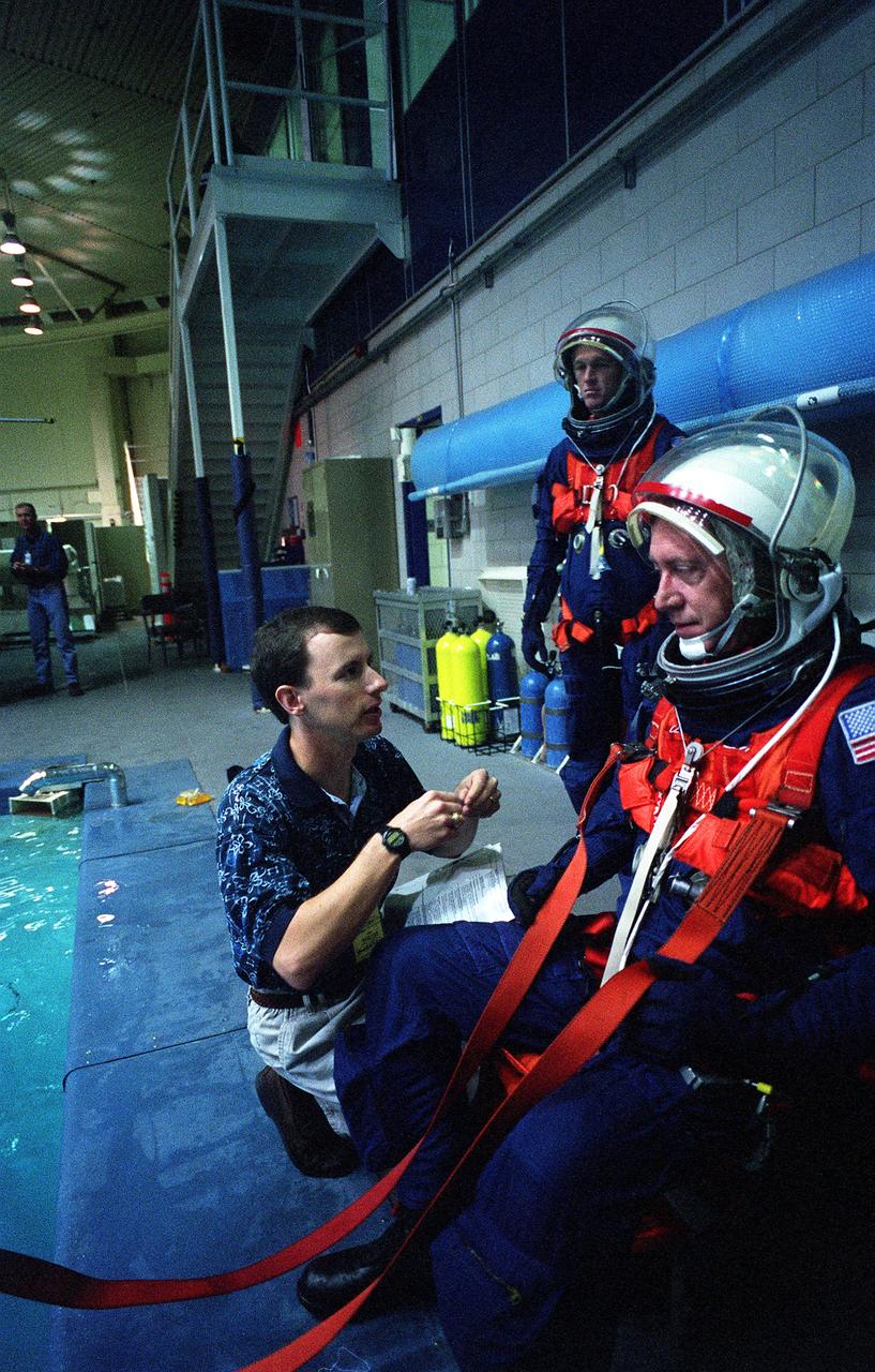 S96-15388 (26 Sept. 1996) --- In the Johnson Space Center's weightless environment training facility, astronaut Michael Baker, STS-81 mission commander, prepares to simulate a parachute drop into water. David Pogue helps with the final touches on Baker's training version of the launch and entry suit, as Brent W. Jett (background), pilot, looks on.