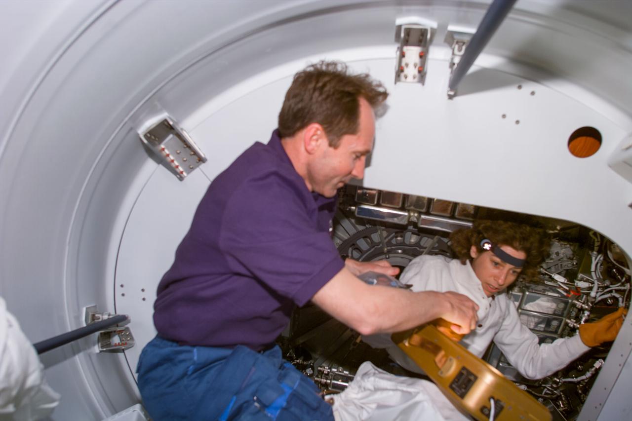 S96-E-5002 (29 MAY 1999) --- With the aid of a lamp, cosmonaut Valery Tokarev and astronaut Ellen Ochoa participate in the activation of SPACEHAB on Flight Day 2.  The photo was recorded with an electronic still camera (ESC) at 07:18:06 GMT, May 29, 1999.