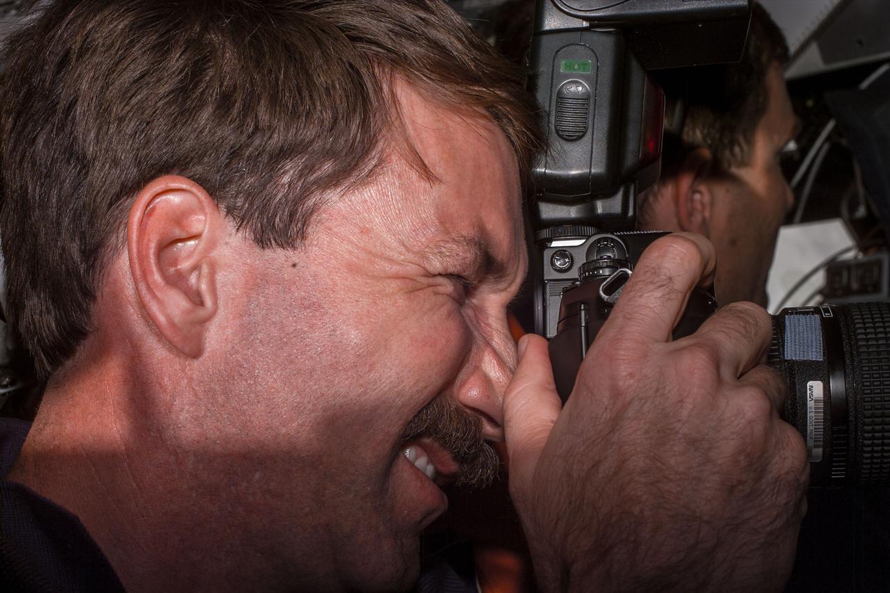 S96-E-5061 (29 May 1999) --- Astronaut Kent V. Rominger, mission commander, takes a picture on Discovery's flight deck shortly after the shuttle had docked with the International Space Station (ISS). Astronaut Rick D. Husband, pilot, can be seen in the background. The photo was taken at 04:38:10 GMT, May 29, 1999.