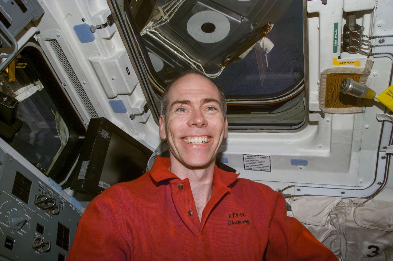 S96-E-5128 (1 June 1999) --- Astronaut Daniel T. Barry, mission specialist, on Discovery's flight deck. Note the docked International Space Station (ISS) visible through overhead window.  The photo was taken with an electronic still camera (ESC) at 11:27:28 GMT, June 1, 1999.