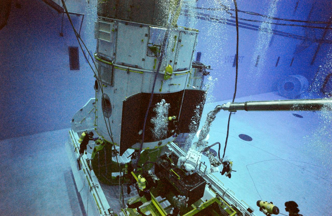 S97-00588 (8 Jan 1997) --- In the new Neutral Buoyancy Laboratory (NBL) at the Sonny Carter Training Center Facility, astronaut Mark C. Lee (obscured by bubbles at center) and an instructor practice procedures to be used during four scheduled space walks to service the Hubble Space Telescope (HST).  At present, four sessions of Extravehicular Activity (EVA), are planned, using two pairs of astronauts on alternating days.  Lee, payload commander, will work with Steven L. Smith, while Gregory J. Harbaugh will team with Joseph R. Tanner.  Astronaut Jeffrey A. Hoffman (wearing space suit, center frame) who performed three EVA?s on the initial HST-servicing mission, helped to train the astronauts.