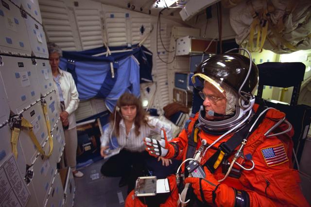 S98-06944 (28 April 1998) --- U.S. Sen. John H. Glenn Jr. (D.-Ohio) prepares to rehearse launch readiness procedures on the middeck of a crew trainer at the Johnson Space Center (JSC). Sharon Jones, involved in crew training, briefs the STS-95 payload specialist. When he lifts off aboard the Space Shuttle Discovery in October of this year and later lands in Florida, Sen. Glenn will be seated in a temporary middeck chair like the one used in this training exercise. The photo was taken by Joe McNally, National Geographic, for NASA.