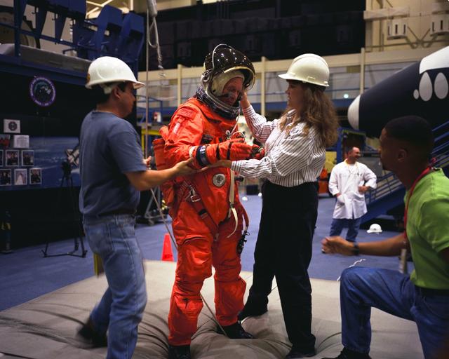 S98-06948 (28 April 1998) --- U.S. Sen. John H. Glenn Jr. (D.-Ohio) receives assistance from crew trainer Sharon Jones and an unidentified staffer in the systems integration facility as he checks his training version of the Shuttle launch and entry garment. Suit expert Carlous Gillis looks on at right. Moments later, the STS-95 payload specialist participated in a rehearsal of an emergency egress from the Space Shuttle. The photo was made by Joe McNally, National Geographic, for NASA.