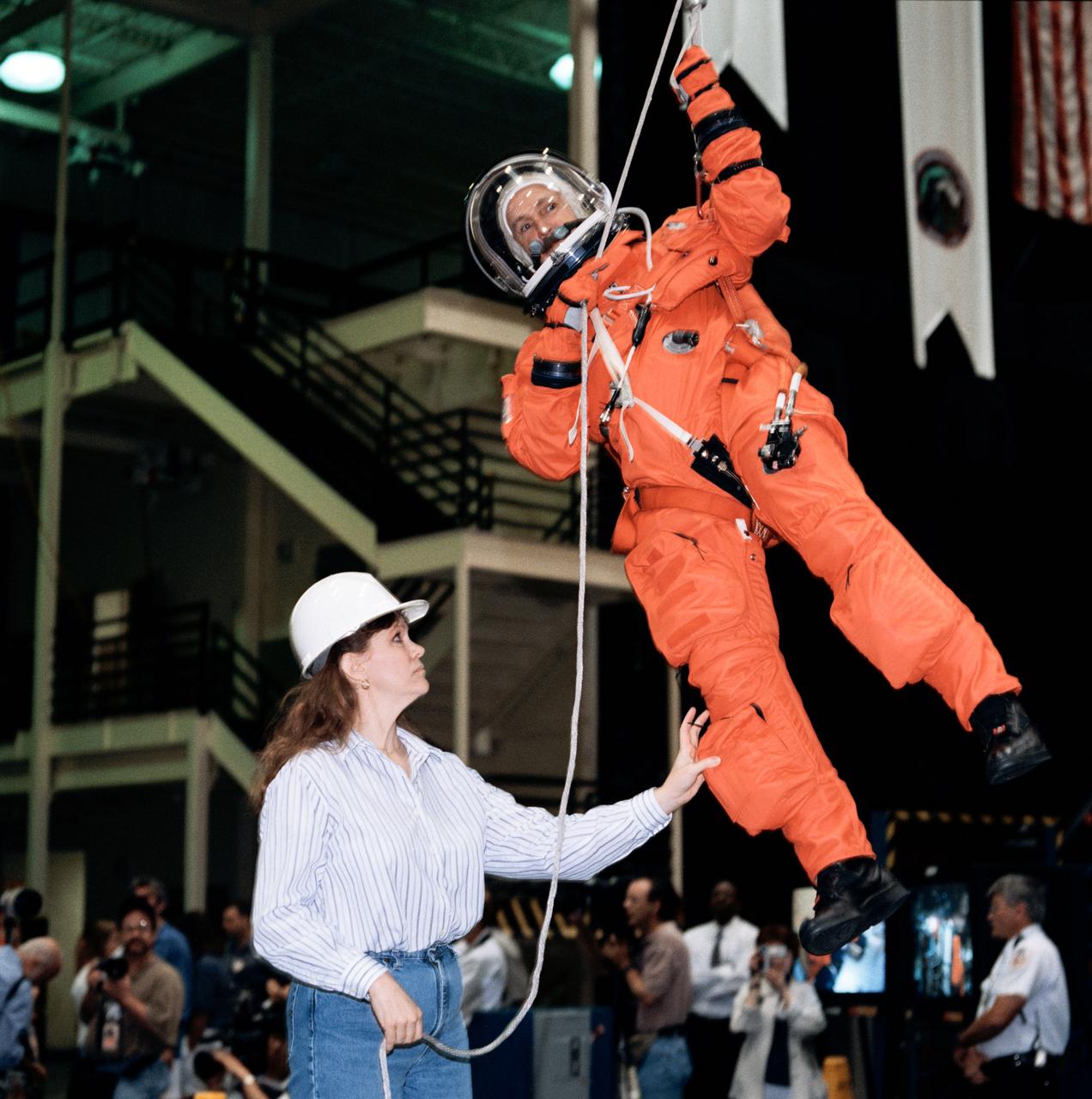 Photographic documentation of the STS-95 crew emergency egress training at the bldg 9A Full Fuselage Trainer (FFT). Views include: Mission specialist Senator John Glenn (in his orange Launch and Landing (LES) suit) is photographed by his wife as other visitors look on (07958). STS-95 crewmember prepares to use the Sky Genie to climb down the side of the FFT (07959). STS-95 crew lines up to pose for pictures in their LES's. Left to right are: Mission specialist Pedro Duque, payload specialist Chiaki Mukai, commander Curt Brown, payload specialist U.S. Senator John Glenn, mission specialist Stephen Robinson, pilot Steven Lindsey, and mission specialist Scott F. Parazynski (07960). Parazynski, Glenn and Robinson talk while their photo is being taken (07961). Mukai receives assistance from suit techs in donning her LES helmet (07962). Glenn receives assistance from suit techs in donning his LES helmet (07963). Glenn, in his LES, walks toward the FFT (07964). Glenn uses the Sky Genie to prepare to climb down the side of the FFT (07965). View of Mrs. Annie Glenn watching her husband during training (07966). Mukai receives assistance from a suit tech with her LES while Glenn watches (07967). Close-up view of Mukai in her LES without a helmet (07968). Glenn and Mukai prepare to strap themselves into their seats in the mockup of the FFT middeck (07969-70). Close-up view of Mukai with her helmet on (07971). Mukai climbs down the rope with help from a technician on the ground (07972). Lindsey, Parazynski, Duque, Mukai and Glenn are photographed seated, waiting for training (07973). Close-up of Duque without his helmet (07974). Close-up of Lindsey with his helmet on, talking to a trainer (07975-6). View of Lindsey climbing down the rope (07977).