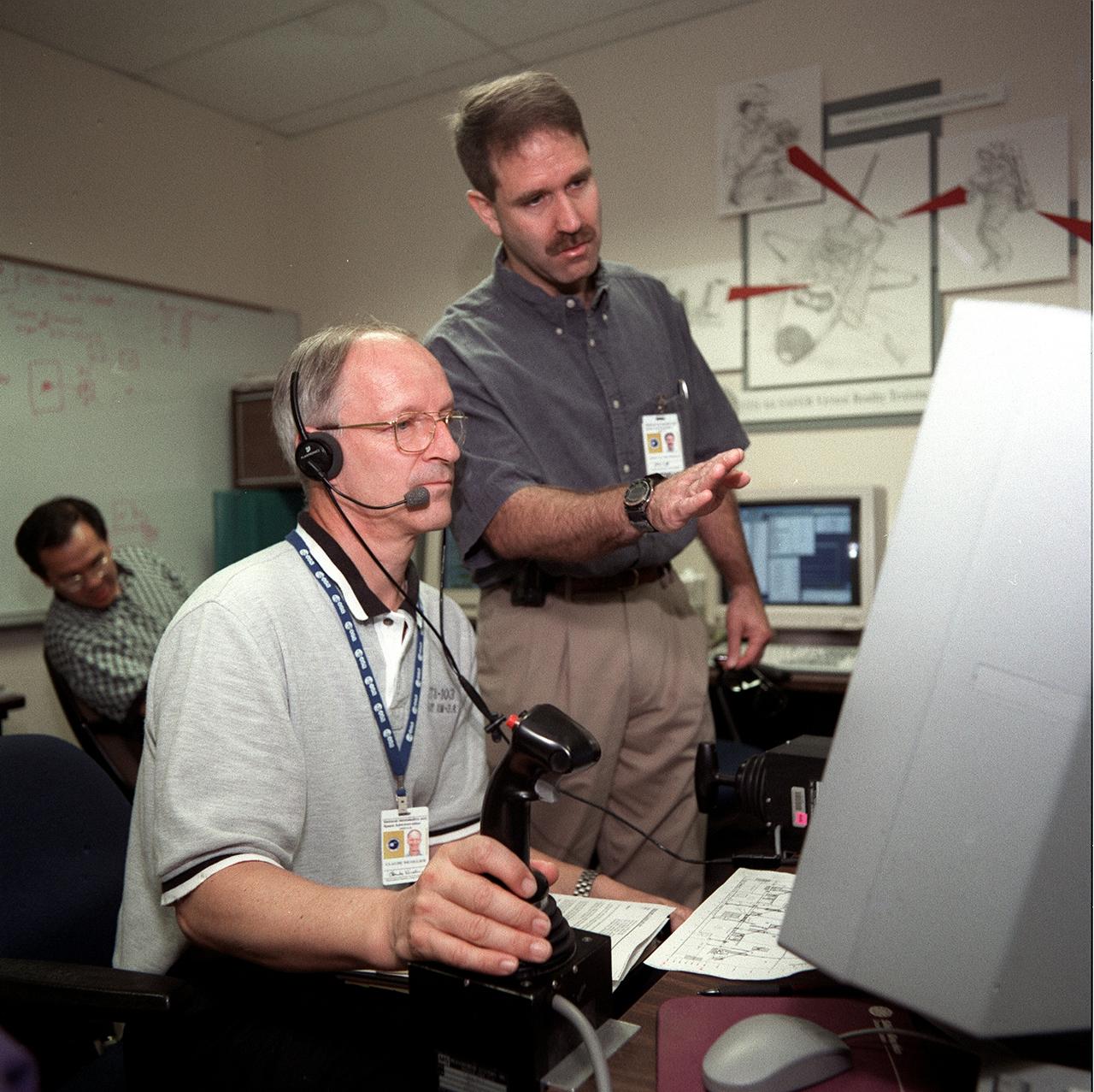 S99-05679 (24 May 1999) --- Astronauts  Claude Nicollier (seated), representing the European Space Agency (ESA), and John M. Grunsfeld use virtual reality  hardware to rehearse some of their duties for the upcoming STS-103 mission, NASA's third servicing visit to the Earth-orbiting  Hubble Space Telescope  (HST).  The two mission specialists will be joined by five other astronauts, including a second ESA representative, for the STS-103 mission, scheduled for autumn of this year.