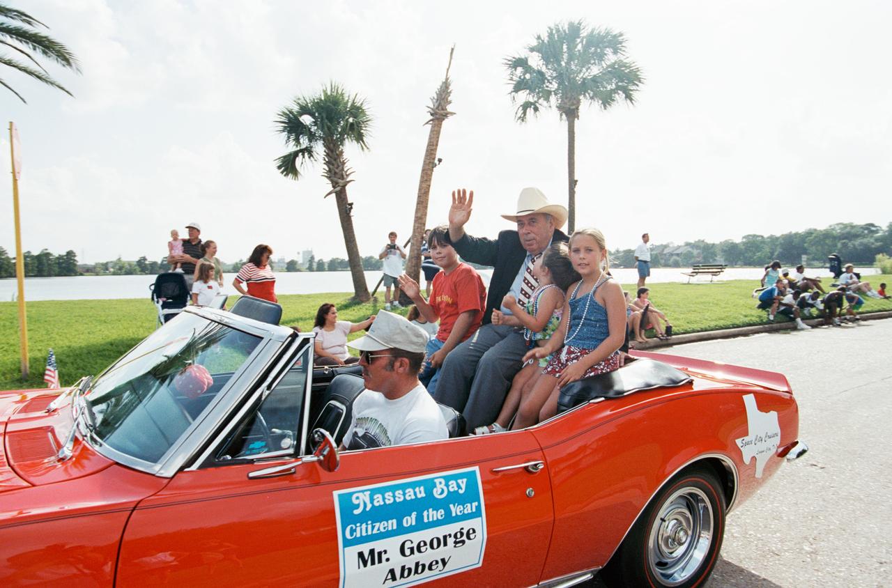 Photographic documentation showing the Nassau Bay July 4th parade honoring George Abbey as "Citizen of the Year." View is of Mr. George Abbey, wearing a cowboy hat, in the back of a car.