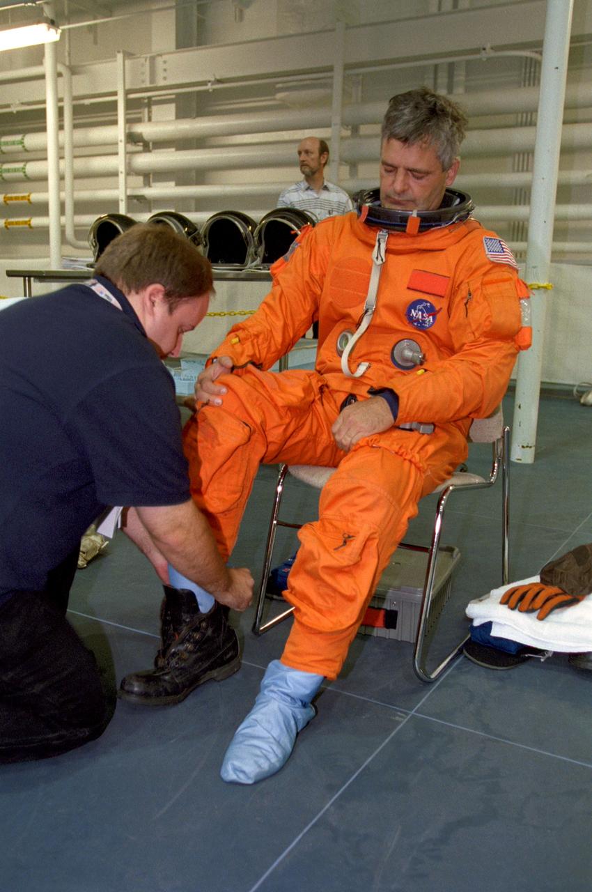 S99-07013 (9 July 1999) --- Astronaut Marc Garneau, mission specialist representing the Canadian Space Agency, with the aid of a United Space Alliance suit technician, dons his shoes while suiting up for a STS-97 training session in the Neutral Buoyancy Laboratory at the Sonny Carter Training Center.