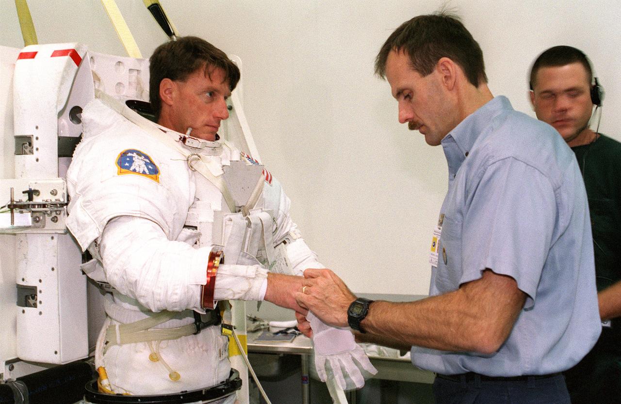 S99-08358 (26 July 1999) --- Astronaut Steven L. Smith (right), mission specialist, assists fellow MS, astronaut C. Michael Foale, with the gloves on his extravehicular mobility unit (EMU) space suit prior to a rehearsal of some of the STS-103 space walk chores in the Neutral Buoyancy Laboratory (NBL). A mockup of part of the Hubble Space Telescope (HST) lies at the bottom of the nearby pool to serve as a prop for the rehearsals of Foale and his crewmates.